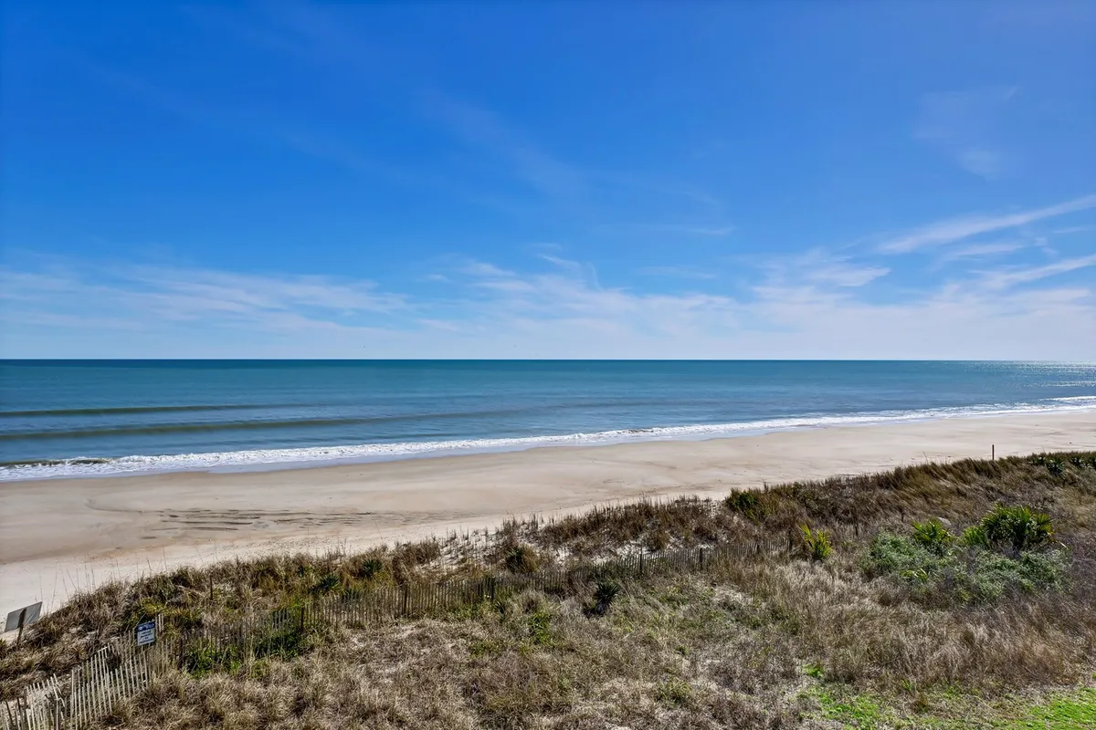 The image showcases a breathtaking view of the wide sandy beach, rolling Atlantic waves, and an expansive blue sky. The serene shoreline invites guests to stroll, sunbathe, or search for seashells, all set against a tranquil coastal backdrop. Soft sunlight and open space evoke a peaceful, inviting mood.