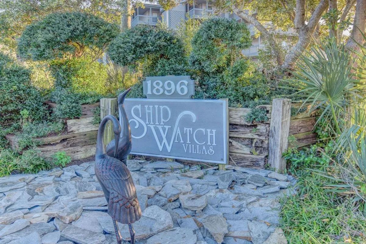 A welcoming exterior shot featuring the Ship Watch Villas sign, a distinctive metal bird sculpture, and well-maintained landscaping. The scene exudes an inviting and peaceful vibe, hinting at the restful escape that awaits within the community.