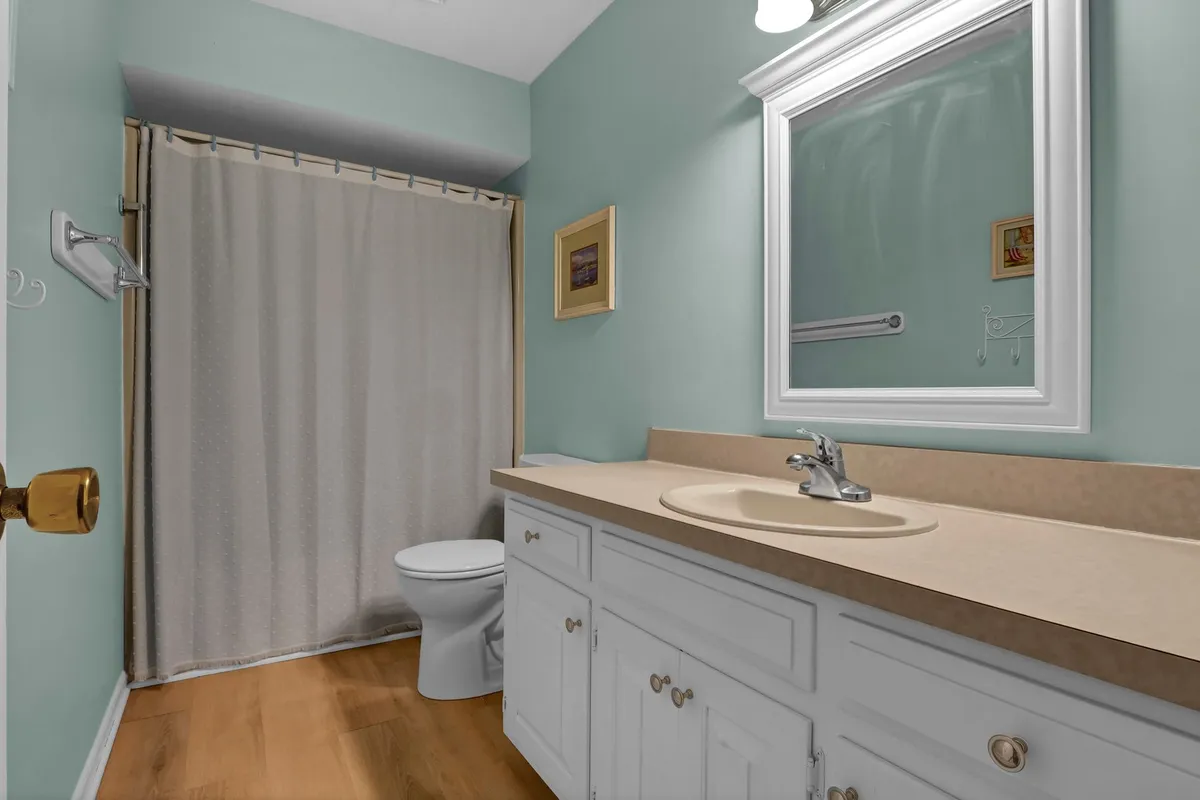 A calming bathroom scene features a modern vanity with a sink, a bright mirror, and subtle framed artwork on the wall. Soft lighting and a neutral palette create a spa-like feel, supporting routines of self-care and relaxation.