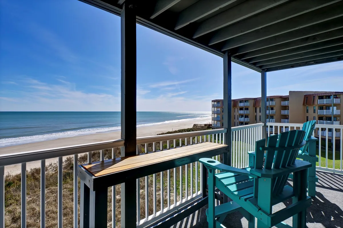 A private balcony with comfortable seating overlooks a sweeping expanse of sandy beach and the rolling ocean. The tranquil view captures the horizon and the gentle light of either sunrise or sunset, inviting guests to relax, socialize, or simply soak in the coastal ambiance together.