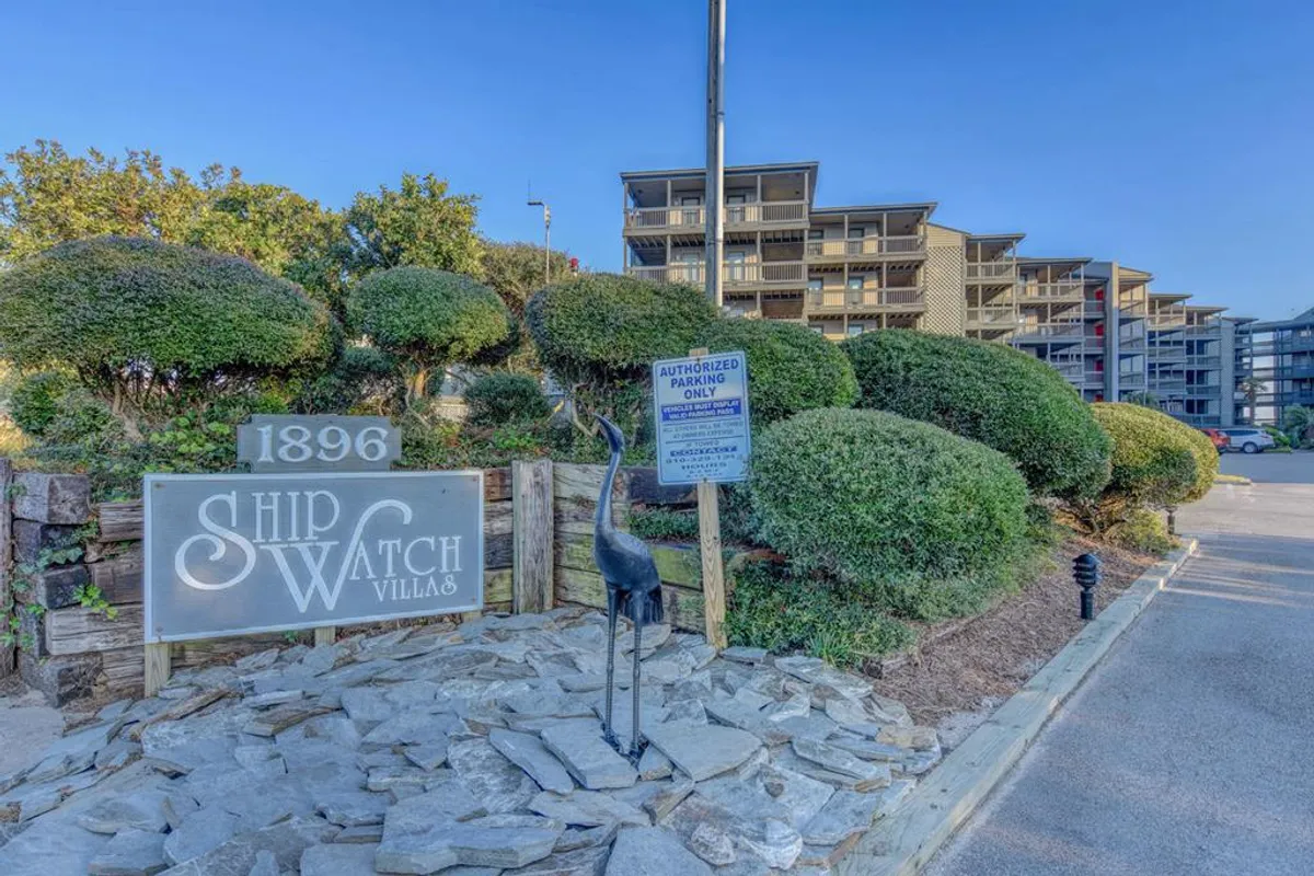Another exterior perspective with the Ship Watch Villas sign, decorative crane statue, and lush greenery. The gentle garden setting suggests opportunities for quiet walks and enjoying nature, supporting the concept of seaside serenity.