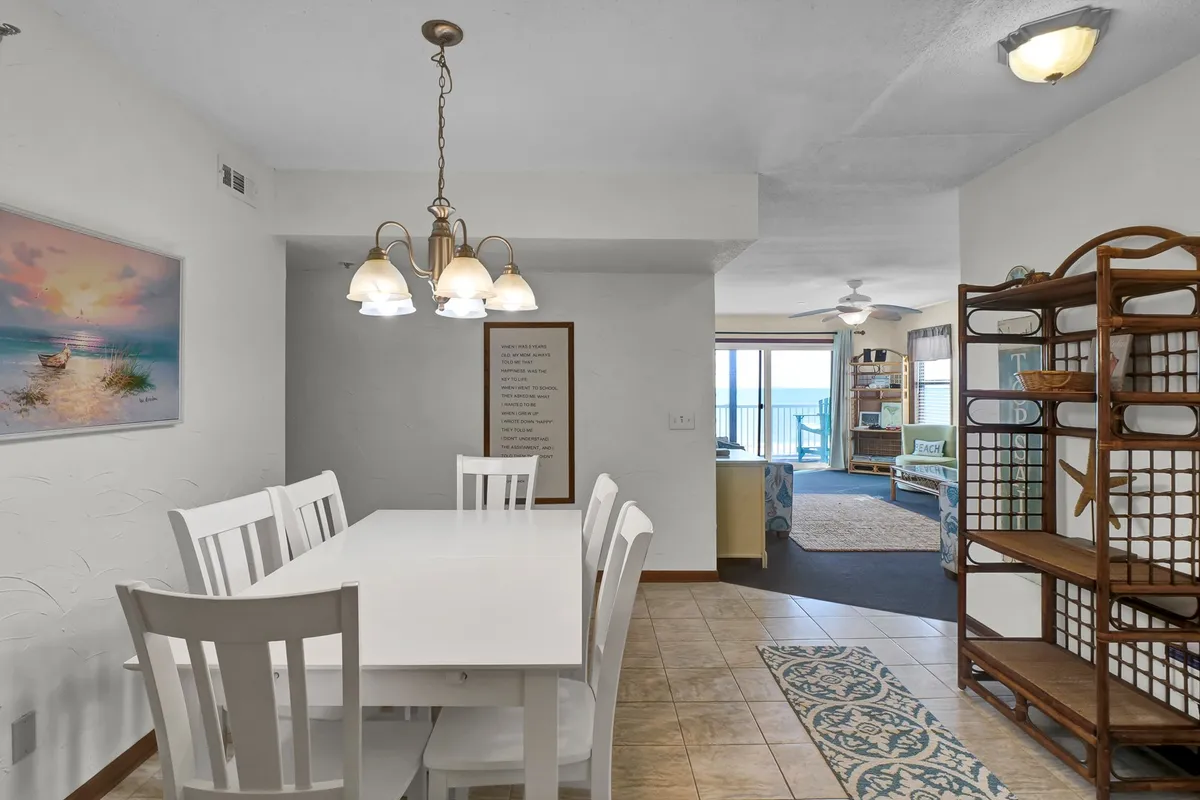 An inviting dining area with a table under a chandelier faces large windows that reveal a stunning ocean view. The space feels open and bright, ideal for working remotely, dining, or relaxing while enjoying the coastal scenery.